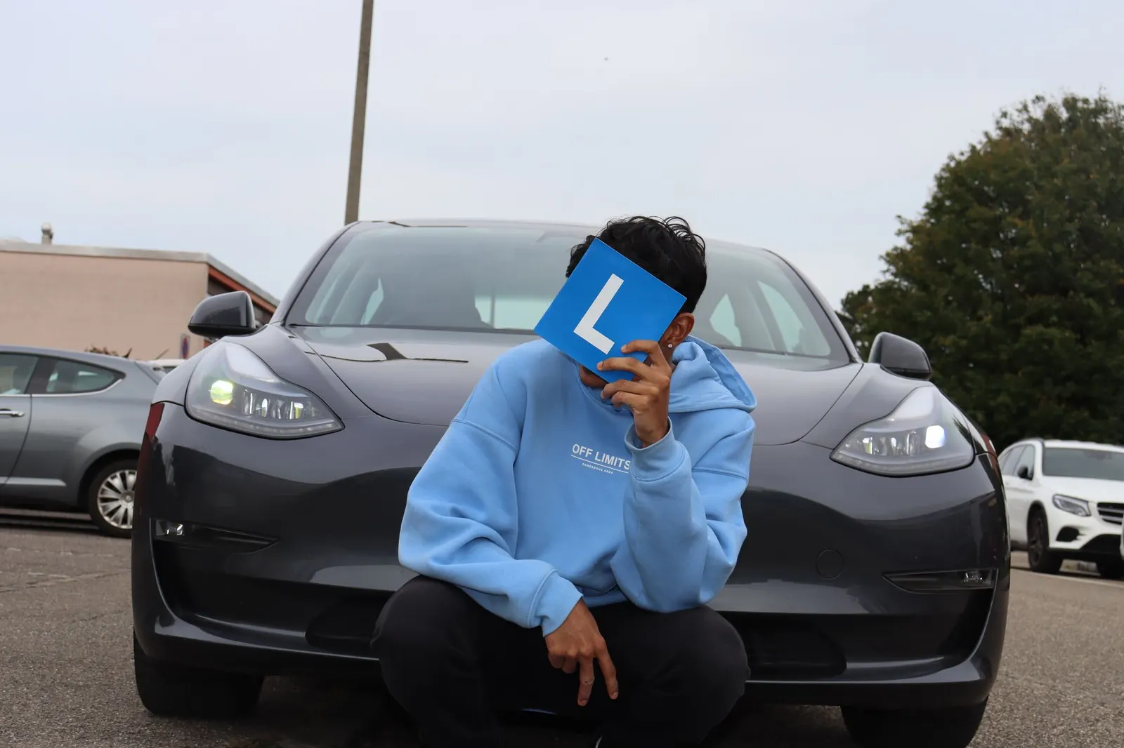 Fahrschüler hält das blaue L-Schild vor dem Tesla